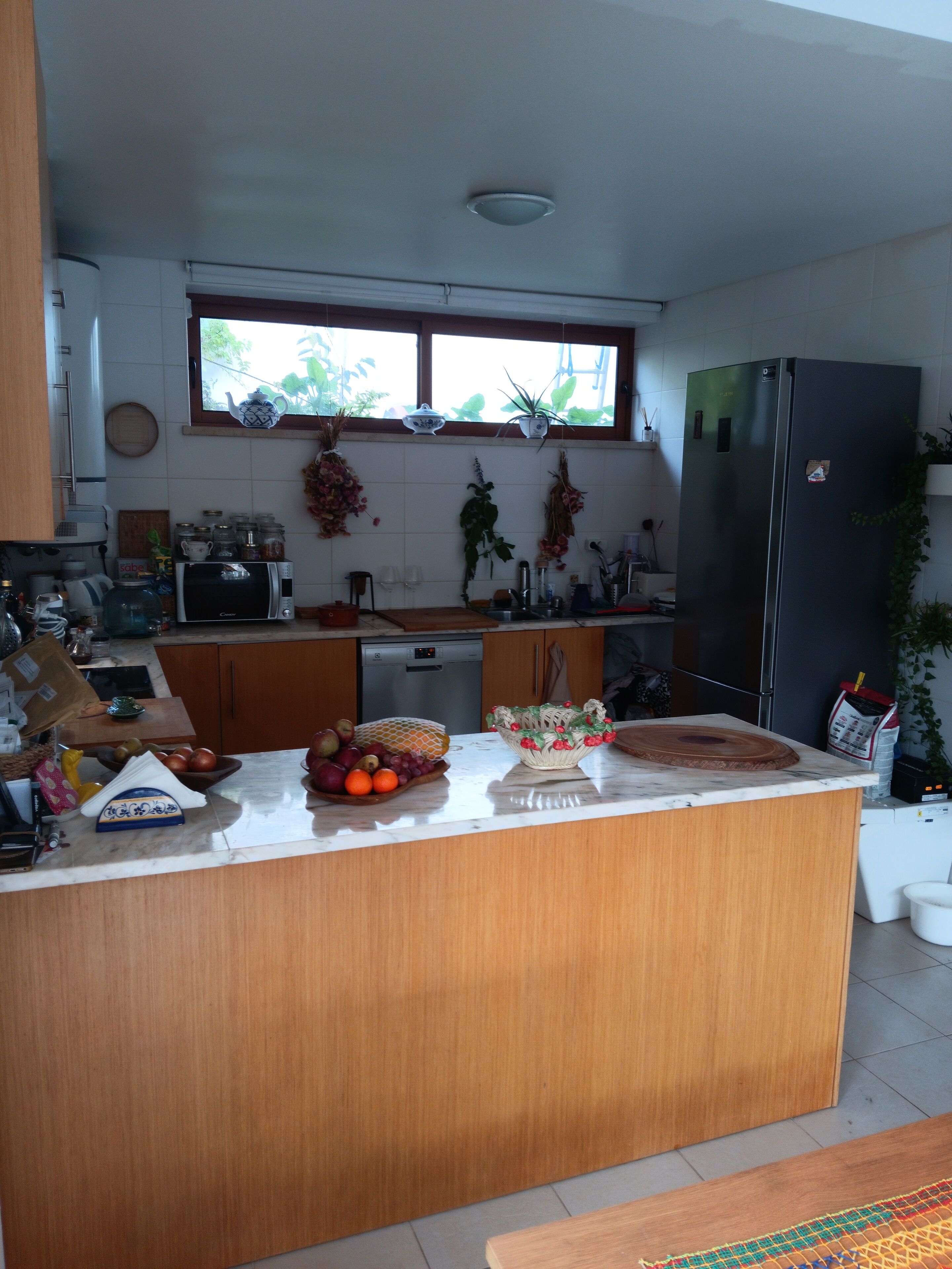 Una cocina moderna con armarios de madera, microondas integrado, refrigerador y una ventana con plantas.