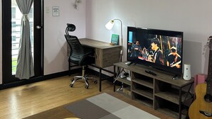 A living room with a wooden desk, a television, a guitar, and a window with curtains. - Welcome to Solstay, a get go place to stay Cozy 1-bedroom condo near Alabang (Muntinlupa)