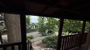 A covered porch with a view of a residential area, including a house and a driveway.