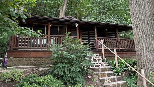 A rustic cabin with a wooden staircase leading up to a porch, surrounded by lush greenery and trees.