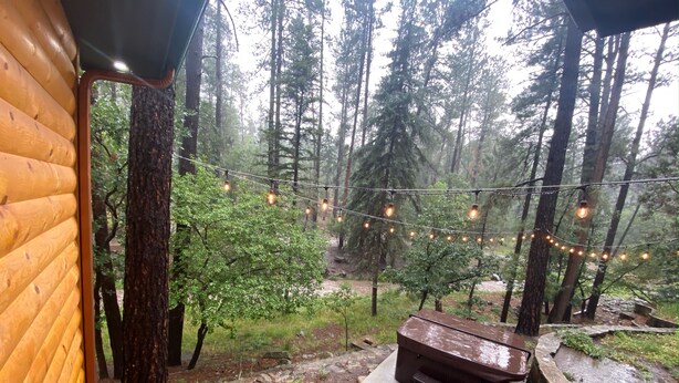 A wooden cabin with a stone fireplace, outdoor seating, and string lights.
