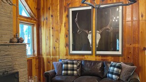 A cozy living room with a fireplace, leather sofa, patterned rug, and wooden walls.