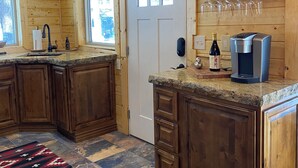 A wooden cabin kitchen with a granite countertop, wooden cabinets, a coffee maker, wine bottle, and a wine glass rack.