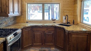 A kitchen with wooden cabinets, granite countertops, a stove, and a window with a view of trees.