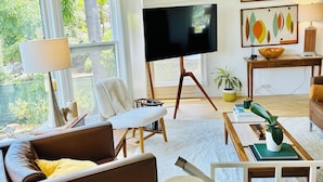 Un salon moderne avec un canapé, une table basse, un téléviseur posé sur un meuble et des œuvres d’art accrochées au mur.