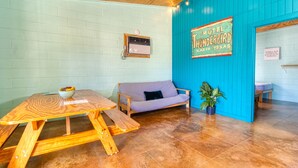 Une pièce avec une table en bois, un canapé à carreaux, un mur bleu orné d’une enseigne de motel et une plante en pot.