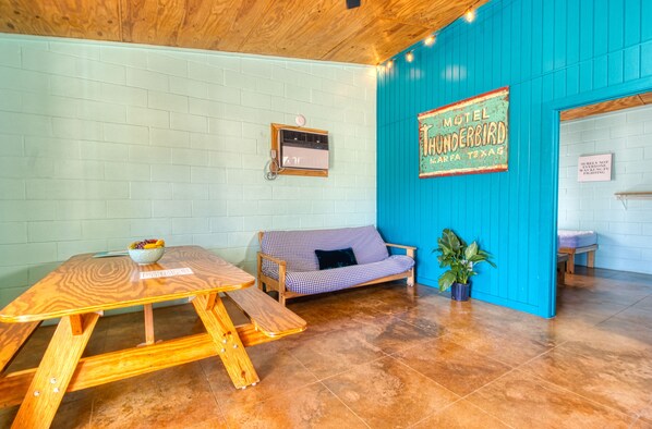 A room with a wooden table, a checkered sofa, a blue wall with a motel sign, and a potted plant. - Nice Little Cabin in the Woods, Frio River Frontage - #3 (Concan)