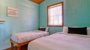 Une chambre avec deux lits, une fenêtre avec des stores à carreaux et un panneau fixé au mur.