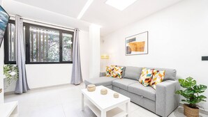 A modern living room with a grey sofa, a white coffee table, and a large window with curtains. - Apartment in Las Palmas Near Las Canteras Beach (Las Palmas de Gran Canaria)