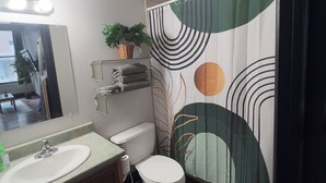 Ein Badezimmer mit Waschbecken, Toilette und einer Duschkabine mit abstrakten Mustern.
