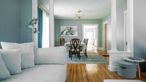 Una sala de estar con un sofá, un comedor con sillas y una mesa, y un pasillo que conduce a otra habitación.