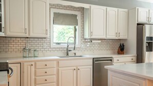 Una cocina con armarios blancos, lavavajillas de acero inoxidable y ventana con vistas a zonas verdes.