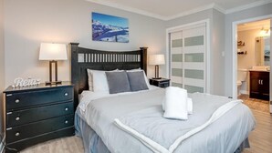 Un dormitorio ordenado con una cama, dos mesitas de noche con lámparas, un aparador y un cuadro en la pared.