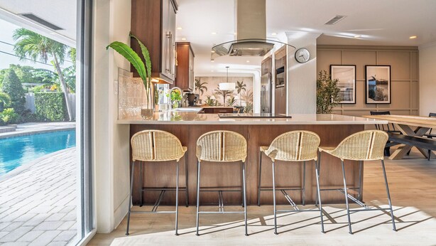Una cocina moderna con barra, una mesa de comedor y vista a una piscina.