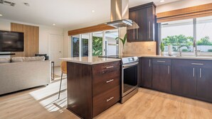Una cocina moderna con armarios oscuros, una campana extractora de acero inoxidable y un amplio ventanal con vistas a la vegetación.