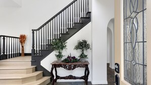 A staircase with a black railing, a console table with potted plants, and a decorative glass door.