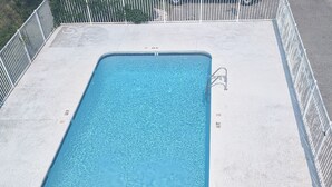 Ein rechteckiger Pool mit einer Metallleiter an einer Seite, umgeben von einem weißen Zaun.