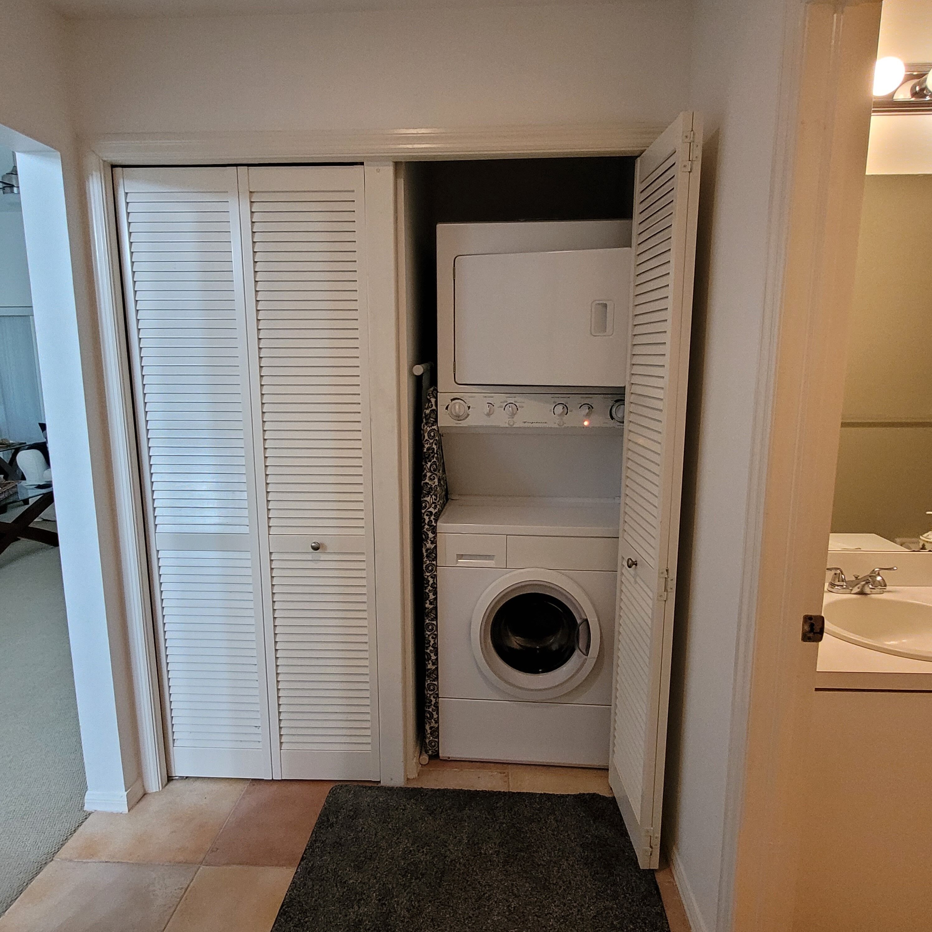 Une petite buanderie comprenant un lave-linge et un sèche-linge, une petite fenêtre et une porte donnant sur une autre pièce.