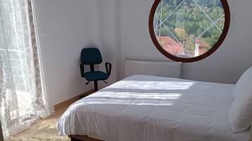 A bedroom with a bed, a chair, a window with a view, and a radiator.