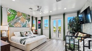 Een moderne slaapkamer met een groot bed, een plafondventilator, een televisie en een balkon met planten.
