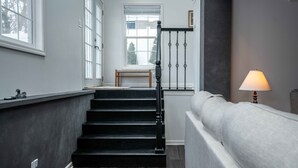 Eine Treppe mit dunklen Holzhäuschen und schwarzen Spindeln, die zu einer Zwischenebene mit einer Bank führt.