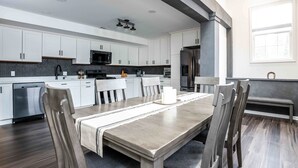 Eine moderne Küche mit weißen Schränken, einem Edelstahlkühlschrank und einem Essbereich mit Holztisch und Stühlen.