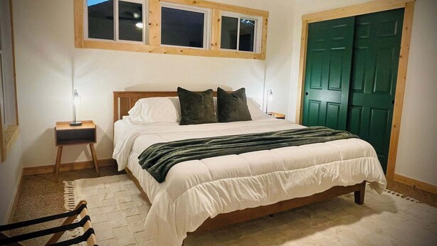 Un dormitorio con cama, mesitas de noche, una puerta verde y una ventana de tres ventanales.