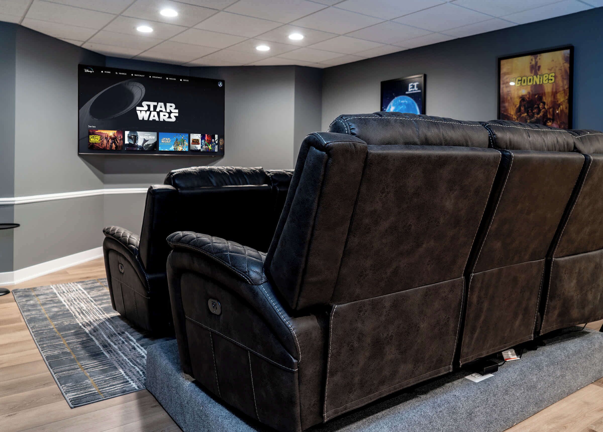 Un home theater con un grande schermo che mostra la serie Star Wars, un divano in pelle reclinabile e un poster del film 'ET'.