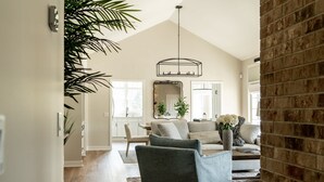 Un soggiorno spazioso con soffitto alto, un grande lampadario e una parete decorata in mattoni.