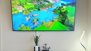 A flat-screen TV mounted on a wall above a white cabinet with a small potted plant and a decorative item.