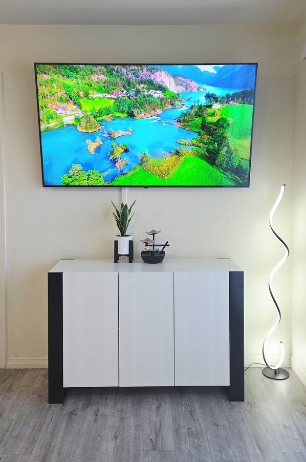 A flat-screen TV mounted on a wall above a white cabinet with a small potted plant and a decorative item. - ⭐️⭐️⭐️⭐️⭐️ Sleek Design. Elevated Stay｜15 min to Downtown! ✅️ (Las Vegas)