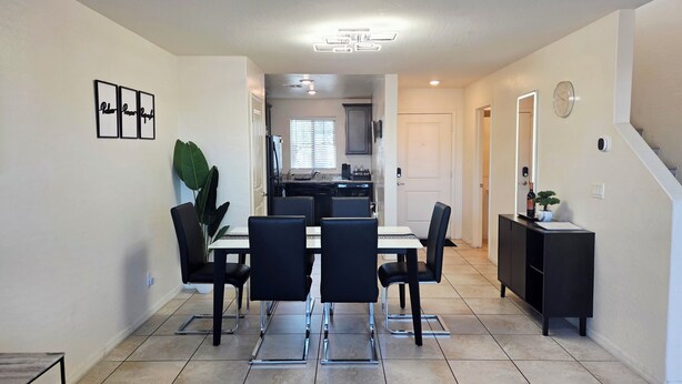 A dining area with a table and chairs, a kitchen in the background, and a staircase leading to another level.