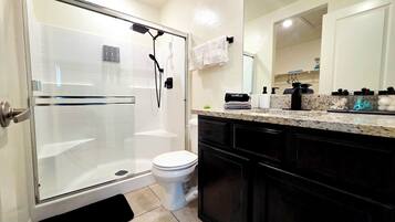 Een moderne badkamer met een douchecabine van glas, een toilet en een wastafelmeubel met wastafel en aanrechtblad.