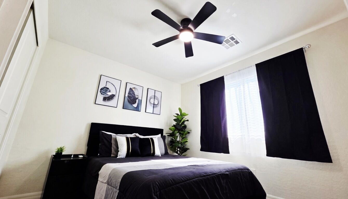 Un dormitorio con cama, ventilador de techo, ventana con cortinas y decoración en la pared.