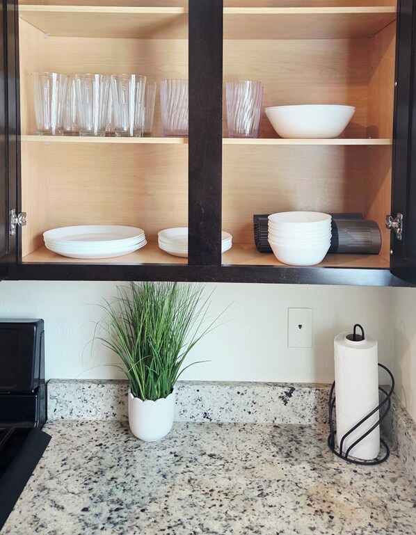 Una cocina con un armario de madera que contiene cristalería, platos y cuencos. Hay una planta en maceta sobre la encimera y un dispensador de toallas de papel.