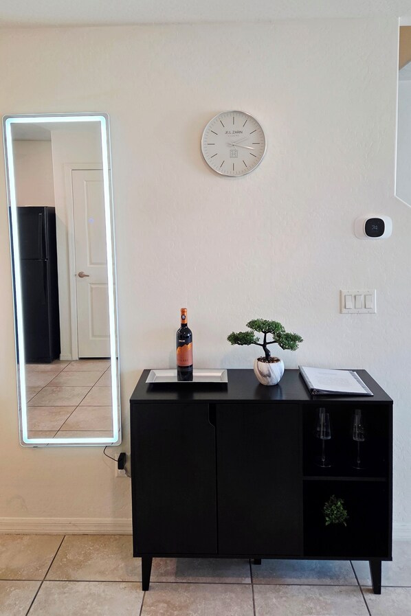 Una habitación con un armario negro, un reloj de pared, una planta en maceta y una botella de vino.