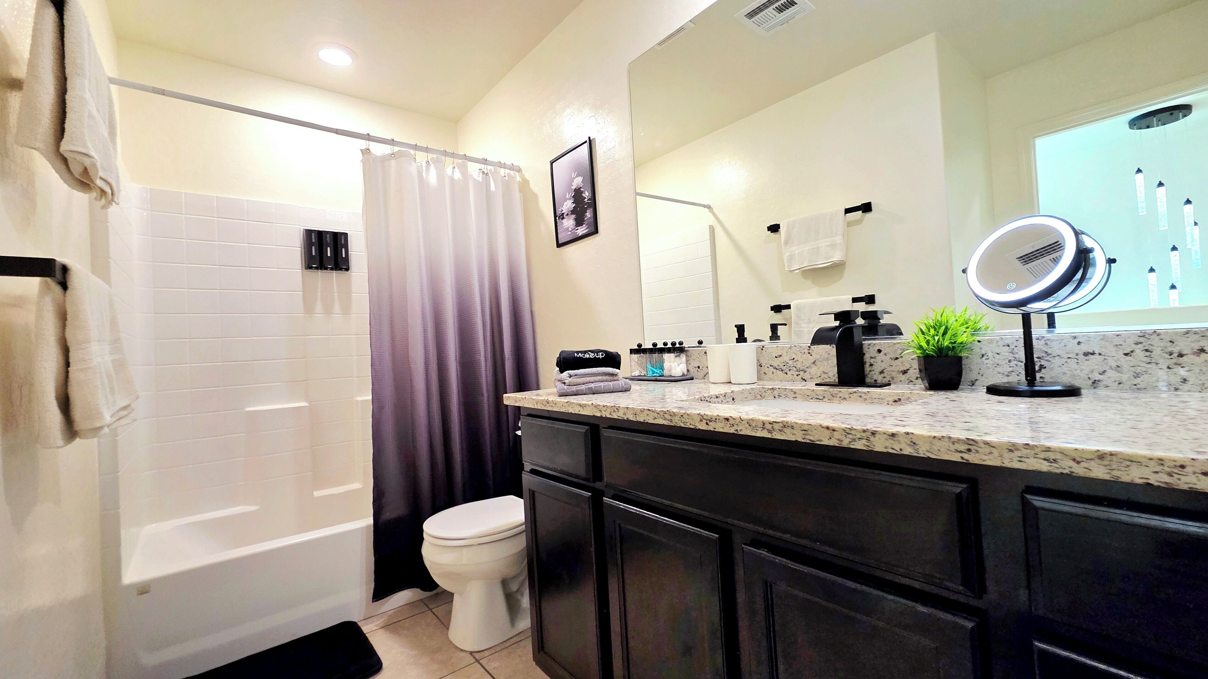 A bathroom with a toilet, a shower curtain, a vanity with a mirror, and a sink.
