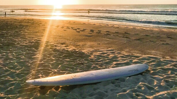 A beach with a surfboard on the sand and the sun setting in the background.