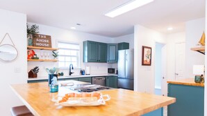A modern kitchen with teal cabinets, a wooden island, and a sign reading "The Shore House".