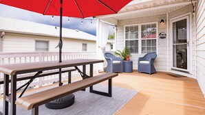 A wooden deck with a picnic table and benches, a red umbrella, and two wicker chairs.
