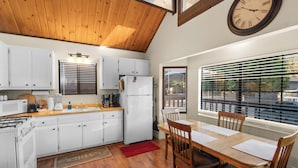A kitchen with white cabinets, a wooden ceiling, a refrigerator, and a dining area with a table and chairs.