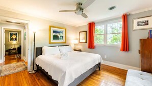 A bedroom with a bed, a nightstand, a lamp, a ceiling fan, and a window with curtains.