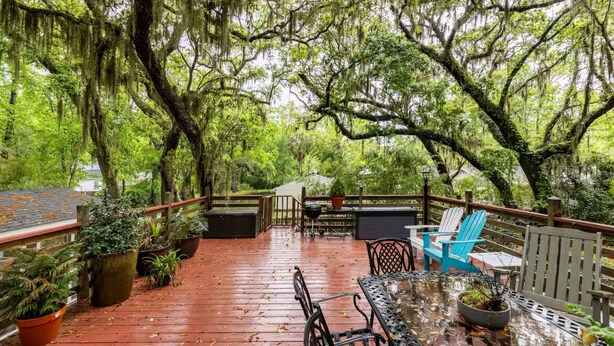 An outdoor deck with a wooden floor, metal chairs, a table, and potted plants.