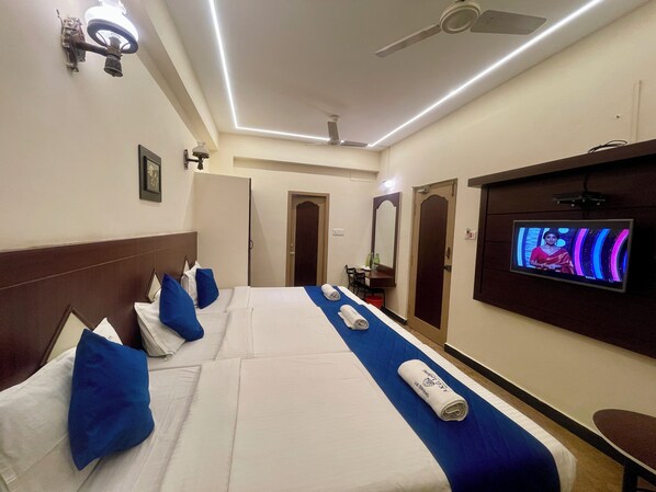 Habitación de hotel con dos camas, televisión, ventilador de techo y puerta al baño.