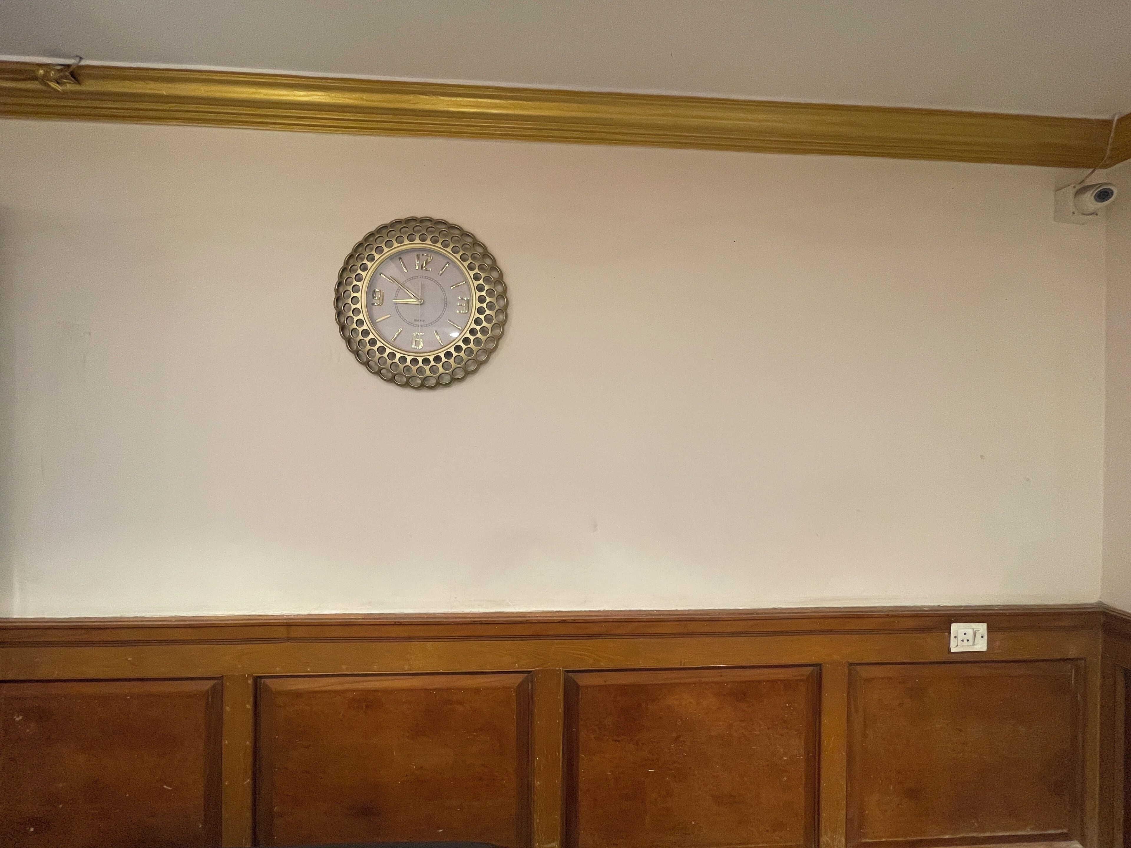 A room with a wall-mounted clock, wooden paneling, and a plain white wall.