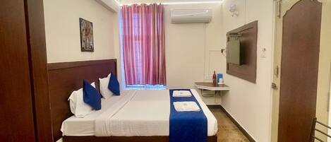 Una habitación de hotel con cama, escritorio, silla, aire acondicionado y televisor.