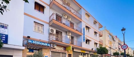 Un immeuble à plusieurs étages doté de balcons, une devanture portant l’inscription « SERRAMAR » et un panneau indiquant une limite de vitesse de 20.