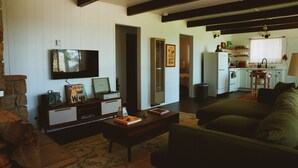 A living room with a television, a coffee table, and a sofa. There is a kitchen area with cabinets and a sink. - The Crescent Moon Cabin with Lakeviews & Wood burning Fireplace (Crestline)