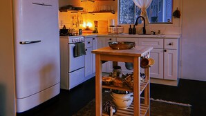 A compact kitchen with white appliances, a wooden table, and a window with curtains. - The Crescent Moon Cabin with Lakeviews & Wood burning Fireplace (Crestline)