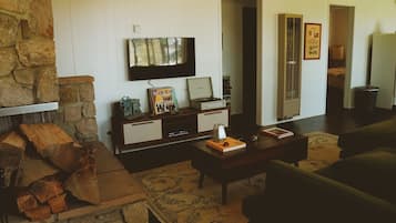 A living room with a stone fireplace, a television mounted on the wall, a wooden coffee table, and a green sofa.